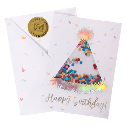 Party Hat Handmade Card, A white card with a die-cut party hat window filled with colorful confetti, silver holographic foil Happy Birthday text, and pom-pom tip-ons, shown with its envelope.