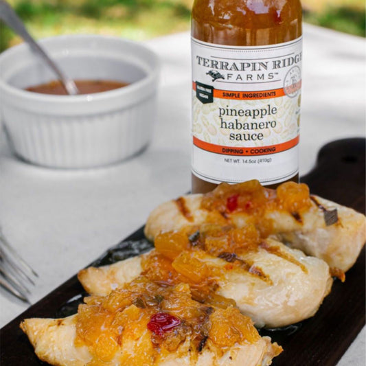 Pineapple and Habanero Sauce, A tall glass bottle of golden pineapple habanero sauce with visible pepper pieces, a black cap and a white label, net weight 14.5 oz.