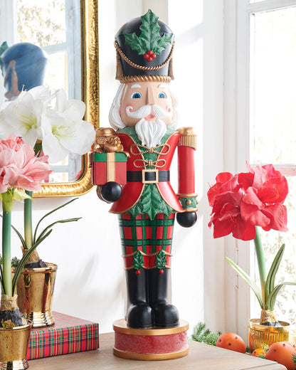 Plaid Nutcracker, A tall resin nutcracker soldier in red and green plaid, holding a wrapped gift and a baton.
