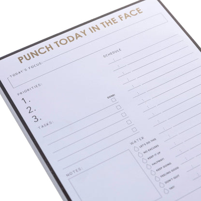 Punch Today Large Notepad, A black-bordered notepad printed 'Punch Today In The Face' in gold foil above sections for priorities, schedule, water, meals, and self-care.