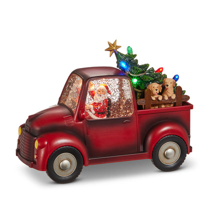 Santa and Pups Lighted Water Truck, A red vintage-style pickup truck with Santa waving inside a glitter-filled cab and two tan pups looking over a wooden rail in the bed beside a small Christmas tree lit with colored bulbs.