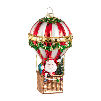 Santa Hot Air Balloon Ornament, A glass ornament showing Santa riding in the basket of a red and white striped hot air balloon with a small tree and gift bag.