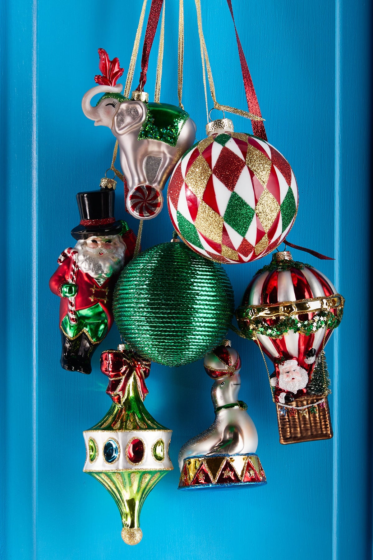 Santa Hot Air Balloon Ornament, A glass ornament showing Santa riding in the basket of a red and white striped hot air balloon with a small tree and gift bag.