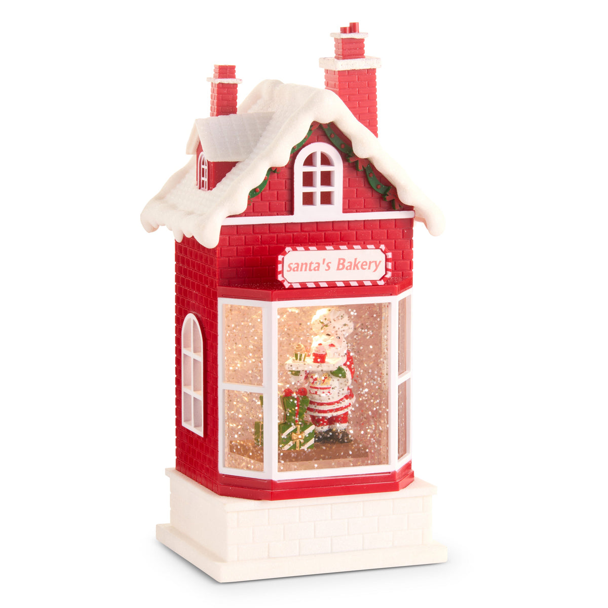 Santa's Bakery Lighted Water Lantern, A red brick bakery lantern lit from inside, with a roof heaped with snow, two chimneys and a sign reading Santa's Bakery, and Santa holding a cookie tray behind a bay window full of glitter.