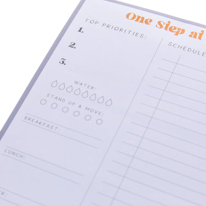 Self Care Large Notepad, A gray-bordered notepad printed 'One Step at a Time' in orange above sections for priorities, meals, water, movement, and self-care.