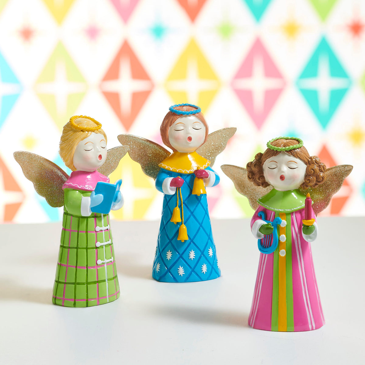 Singing Choir Angel Figurine with Glitter Wings, Three singing angel figurines with glittered gold wings and halos, one in a green plaid robe holding a songbook, one in a pink striped robe holding a lyre and a candle, and one in a blue snowflake robe holding bells.
