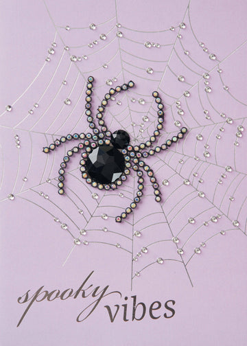 Spooky Vibes Greeting Card, Front of the card showing a spider made of a faceted black gem and small sparkling stones on a silver spiderweb with clear raised droplets above the silver words spooky vibes on a lilac ground.