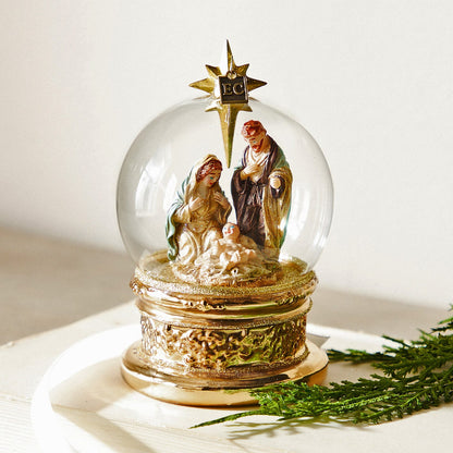 The Blessed Birth Globe Ornament, A clear glass globe ornament with a nativity scene of Mary, Joseph and the baby, set on a gold toned base.