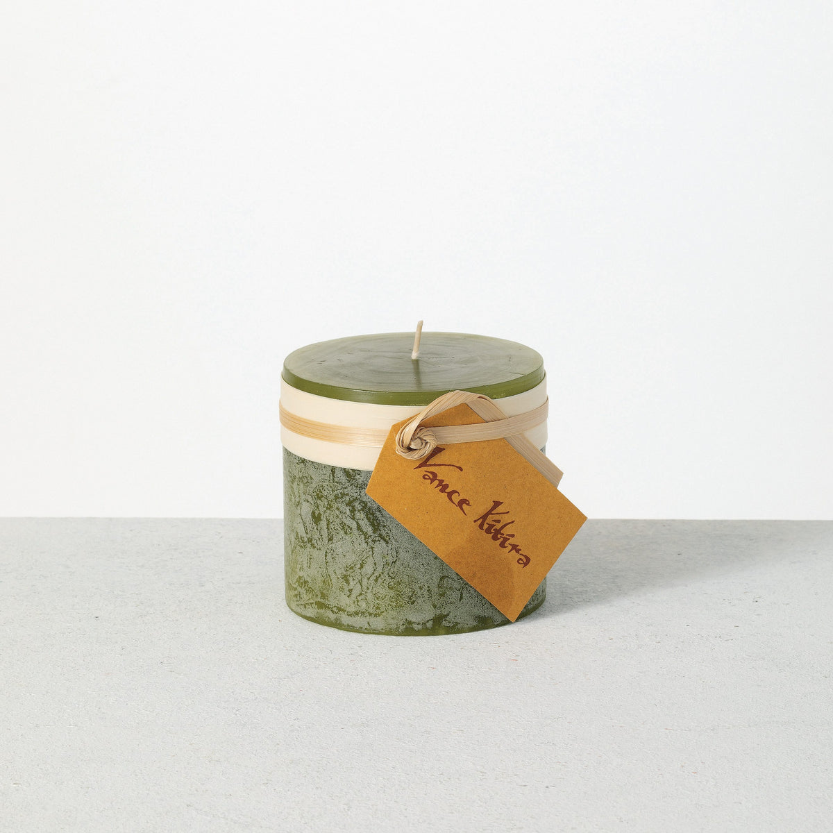 Timber Pillar Candle 3.25 x 3 Inch, A short pillar candle in warm honey gold sits on a plain background with a cream band and a paper tag around its middle.