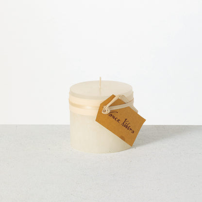 Timber Pillar Candle 3.25 x 3 Inch, A short pillar candle in warm honey gold sits on a plain background with a cream band and a paper tag around its middle.