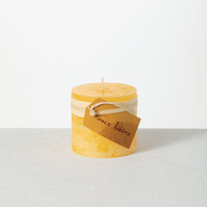 Timber Pillar Candle 3.25 x 3 Inch, A short pillar candle in warm honey gold sits on a plain background with a cream band and a paper tag around its middle.