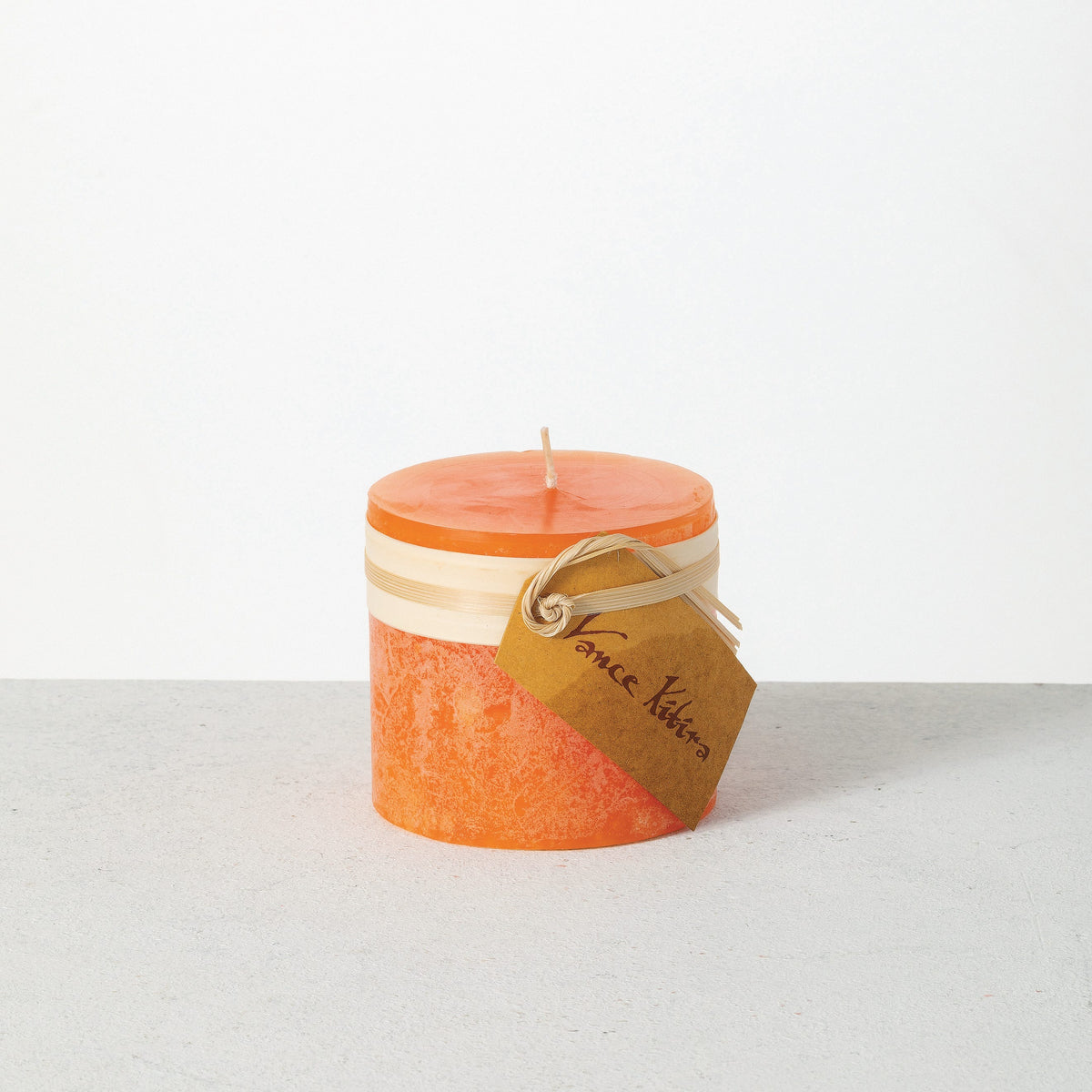 Timber Pillar Candle 3.25 x 3 Inch, A short pillar candle in warm honey gold sits on a plain background with a cream band and a paper tag around its middle.