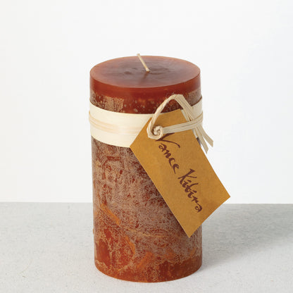Timber Pillar Candle 3.25 x 6 Inch, A tall reddish brown pillar candle with a textured surface stands tied with a paper band and a hang tag.