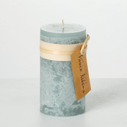 Timber Pillar Candle 3.25 x 6 Inch, A tall reddish brown pillar candle with a textured surface stands tied with a paper band and a hang tag.