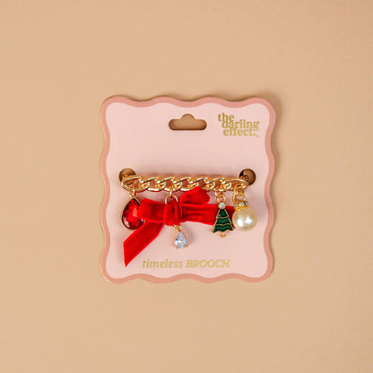 Timeless Brooch, A small gold brooch pin shaped like a teddy bear and covered edge to edge in clear rhinestones, with a gold bow at its neck, shown on a tan background.