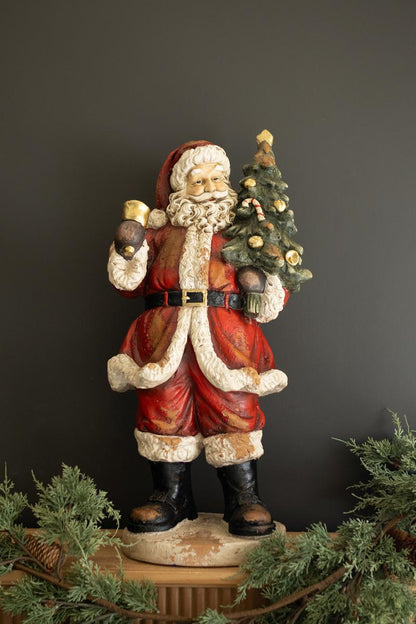 Traditional Faux Concrete Santa with Bell, A tall faux concrete Santa figure in a red suit holding a small Christmas tree.