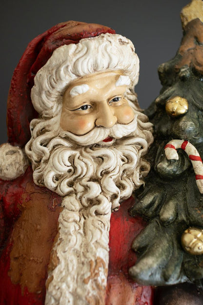 Traditional Faux Concrete Santa with Bell, A tall faux concrete Santa figure in a red suit holding a small Christmas tree.