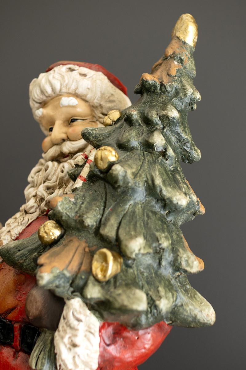 Traditional Faux Concrete Santa with Bell, A tall faux concrete Santa figure in a red suit holding a small Christmas tree.
