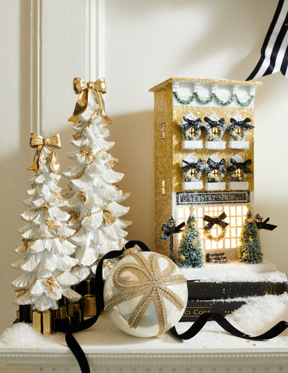 White Bow-Topped Christmas Tree with Presents, White resin Christmas trees in a small and a large size, each topped with a gold bow, trimmed with gold bells, bows and bead garland, and standing on a base of black and gold wrapped presents.