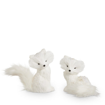 White Winter Fox Figurine, Two white faux fur fox figures with glittered backs, one sitting upright with a long tail and one resting with its tail curled around it.